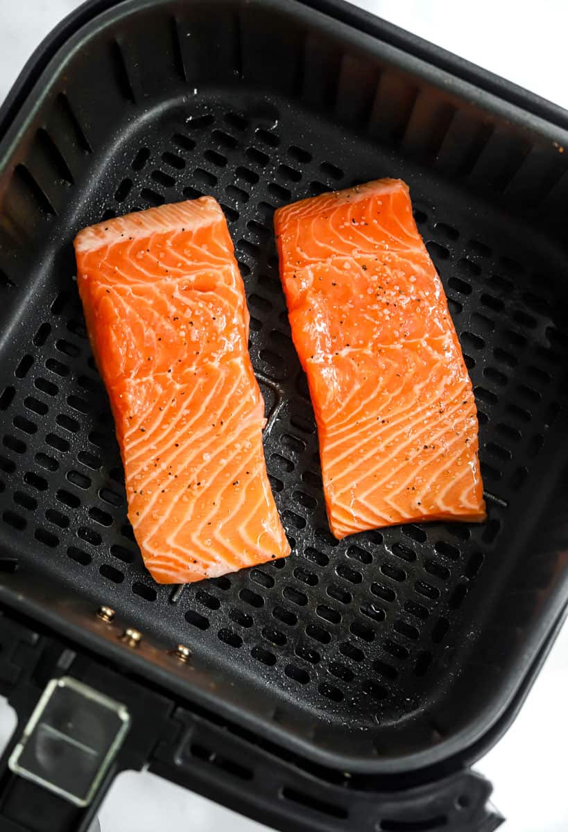 2 seasoned, uncooked pieces of salmon in a black air fryer basket. 