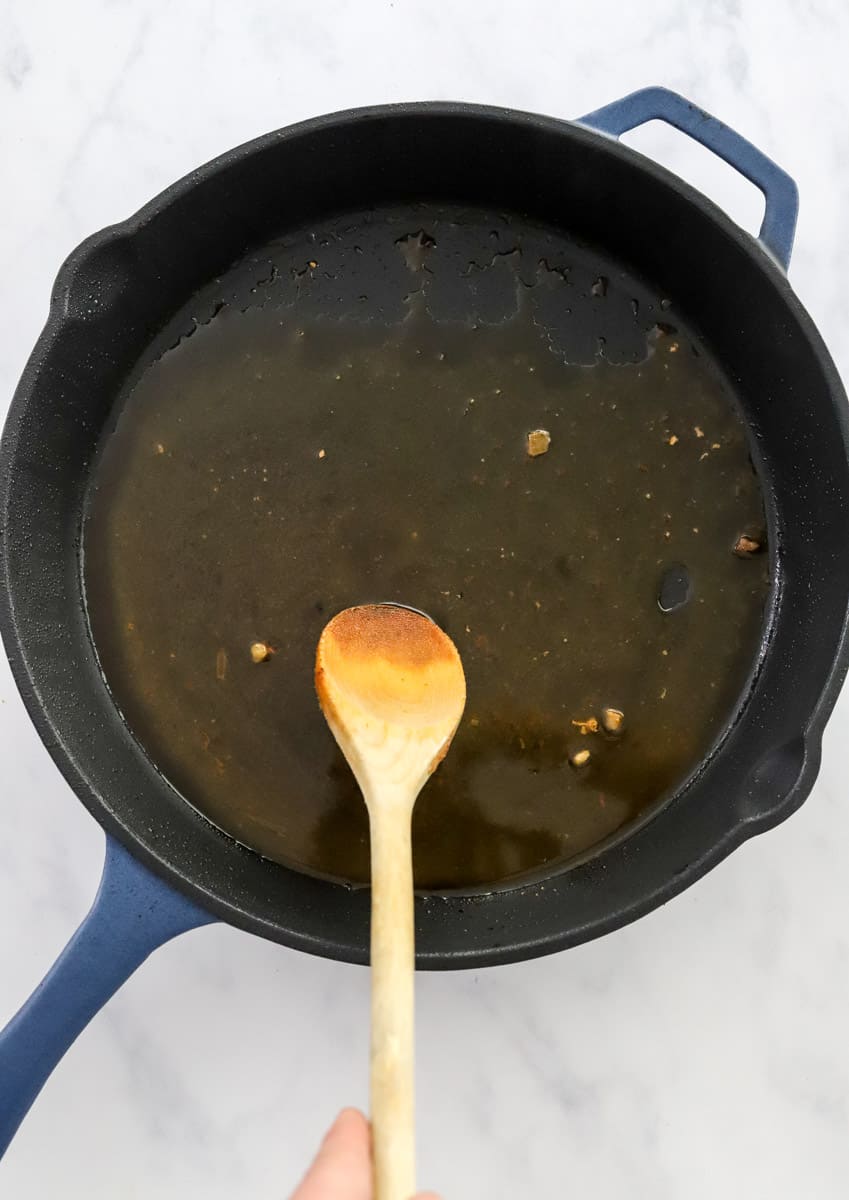 Wooden spoon stirring a brown sauce in a blue cast iron pan. 