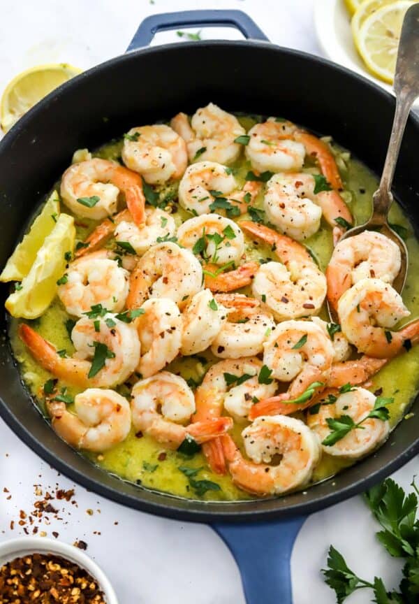 Cast iron pan filled with cooked shrimp scampi in a butter sauce with a spoon in the pan.