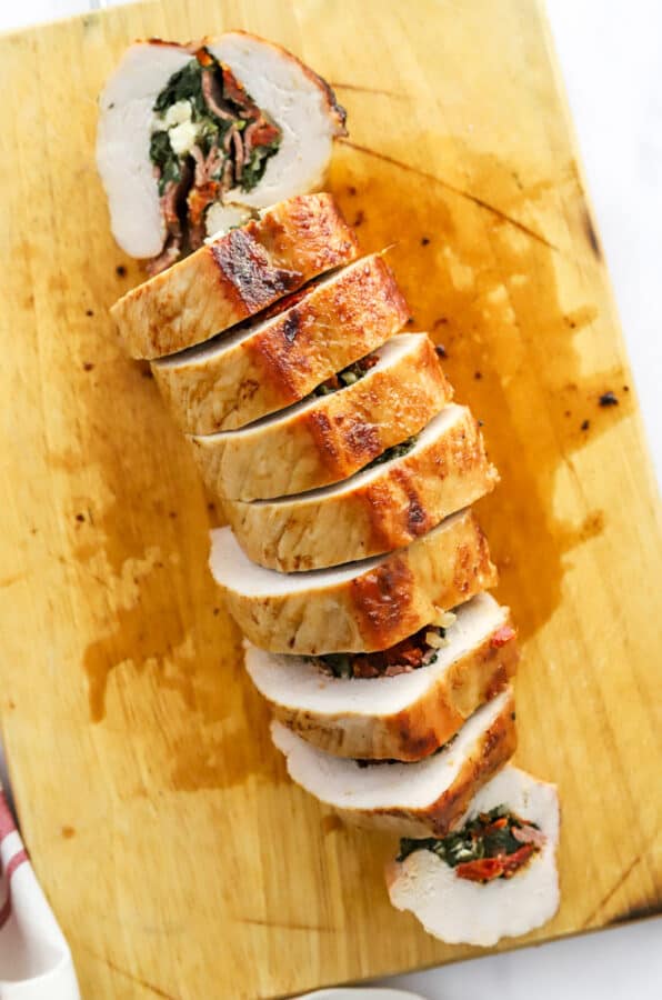 Pork tenderloin with stuffing in it, roasted and sliced on a wooden cutting board.