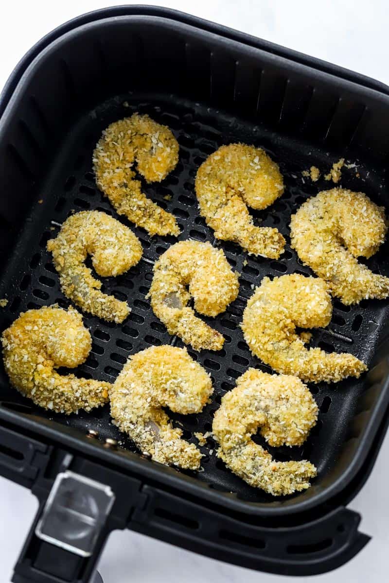 Coated uncooked shrimp in an air fryer basket. 