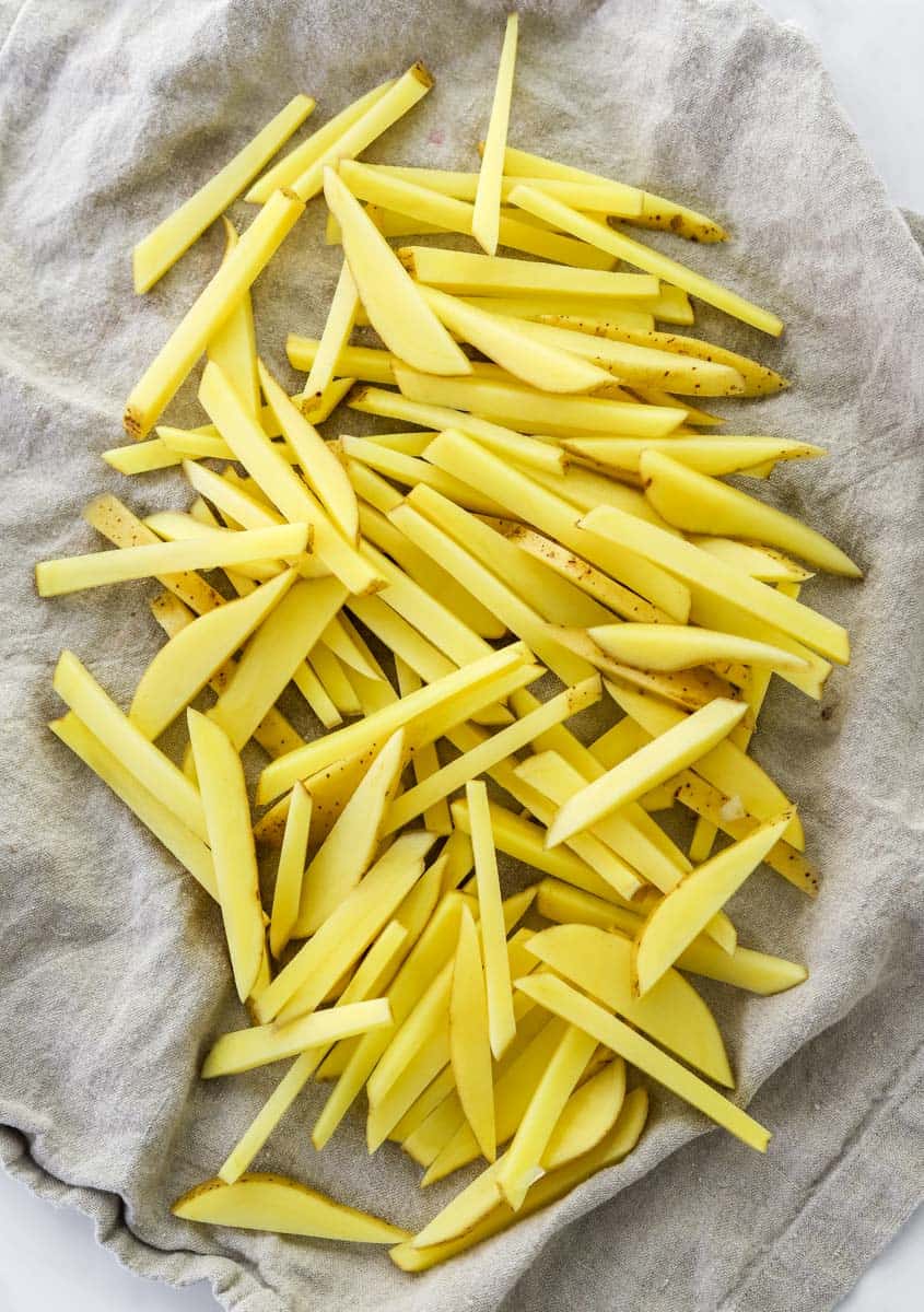 Cut uncooked French fries layer out on a brown kitchen towel.