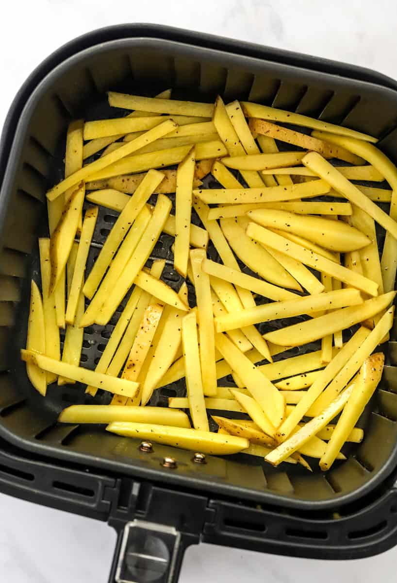 Sliced uncooked potatoes in an air fryer basket.