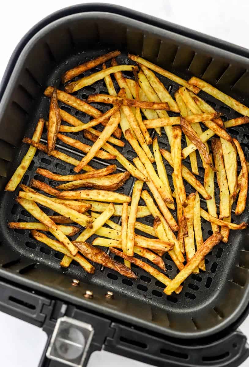 Air fryer French fries cooked in a square, black air fryer basket.