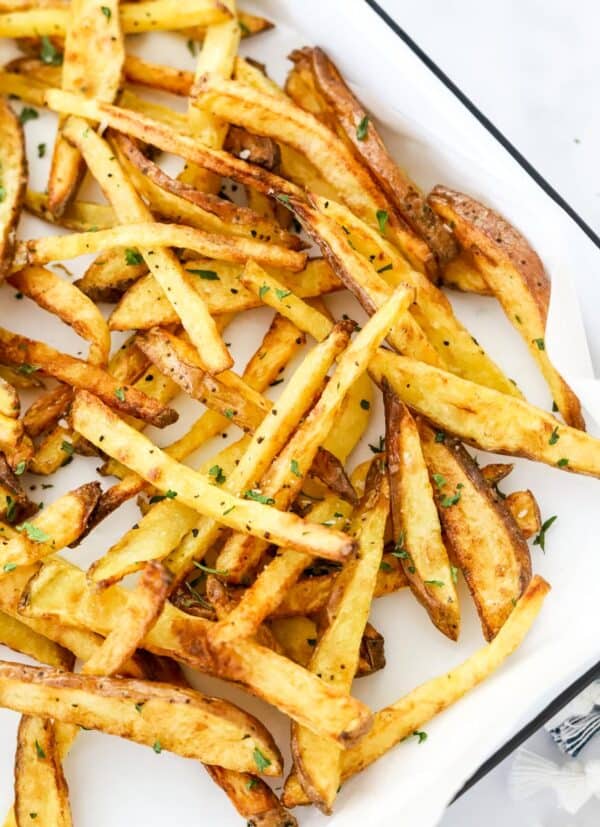 Crispy golden French fries close up on a white and black baking sheet.