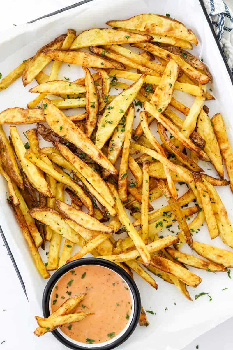 Pile of air fryer fries on a white platter with orange dipping sauce on the platter with them.