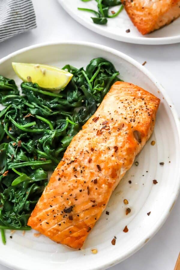 Piece cooked fish on a plate with cooked spinach.