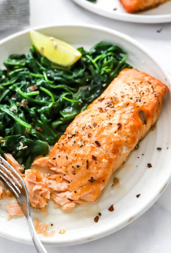 Cooked salmon filet on a late next to cooked spinach with a fork next to it.