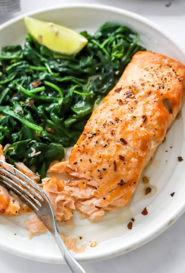 Air fryer salmon on a plate with sautéed spinach with a fork on the plate.