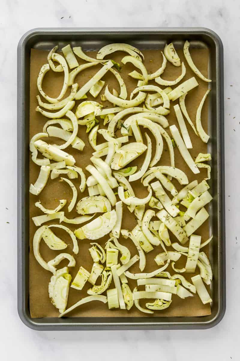 Seasoned, slices of raw fennel on a baking sheet lined with brown parchment paper. 