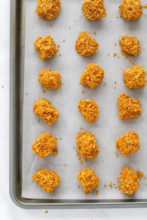 Half a baking sheet with white parchment paper on it with spices of coated chicken on it in rows.