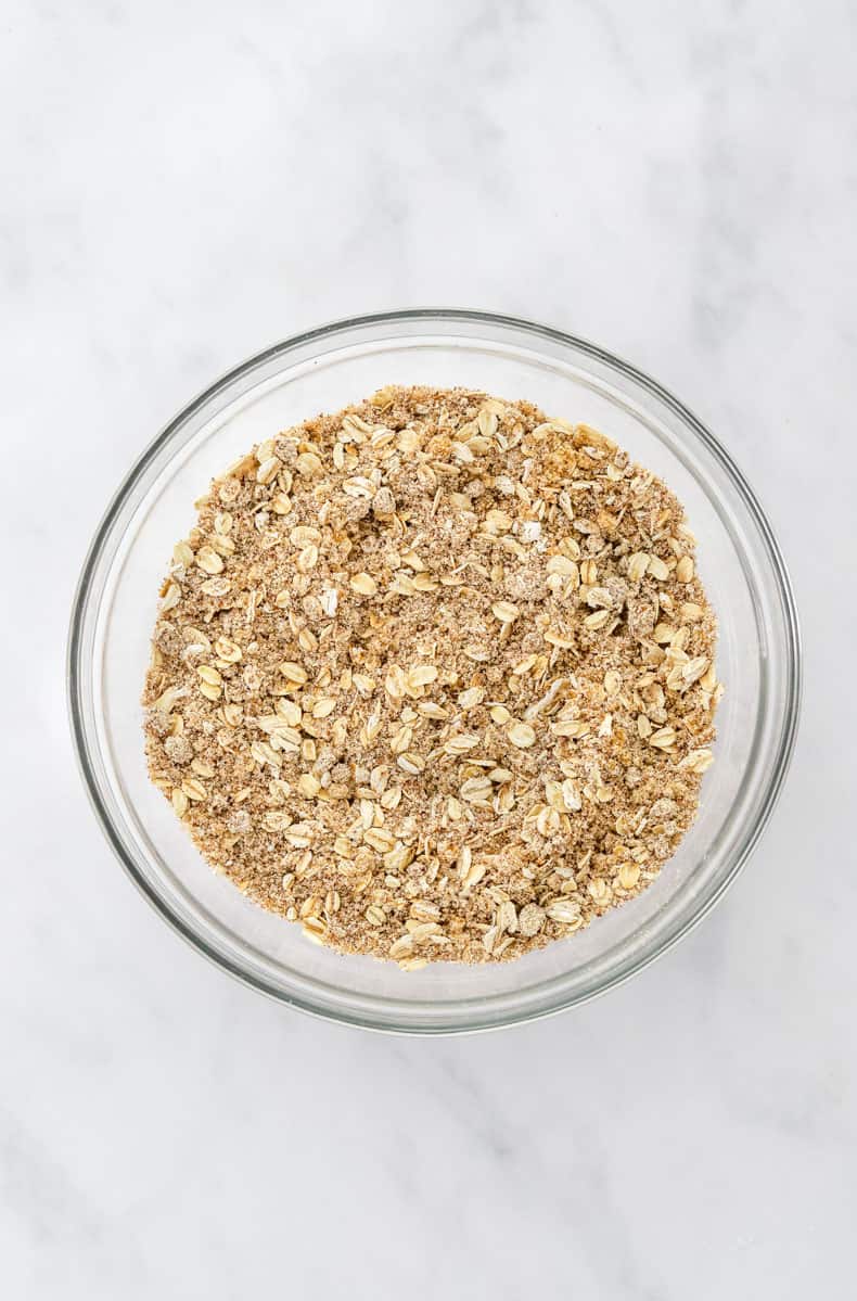 Dry oats and sugar mixture in a glass mixing bowl.