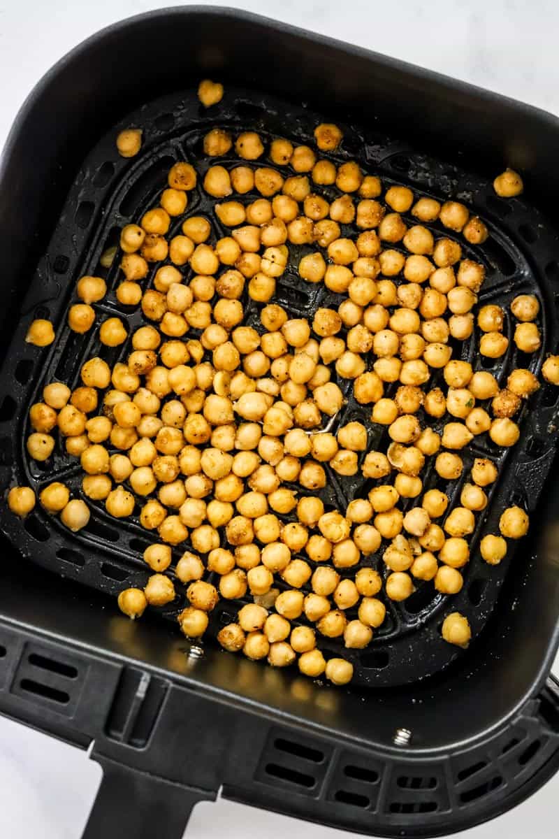Black air fryer basket filled with uncooked chickpeas.