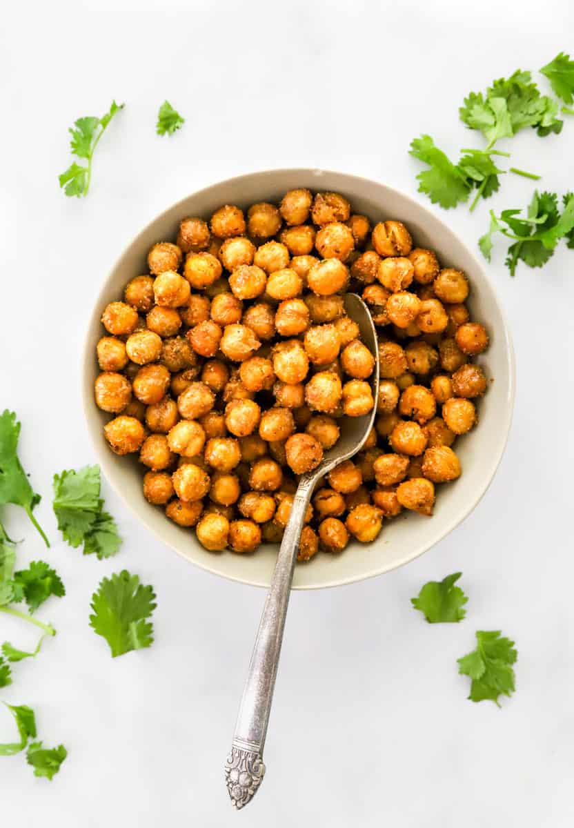 Bowl filled with cooked chickpeas with a spoon in the bowl and torn cilantro around it.