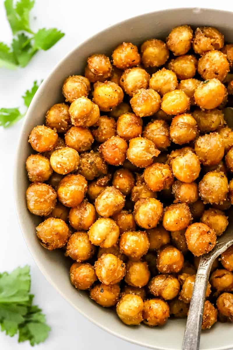 Round bowl filled with crispy air fryer chickpeas with a silver spoon in the bowl and green herbs around it.