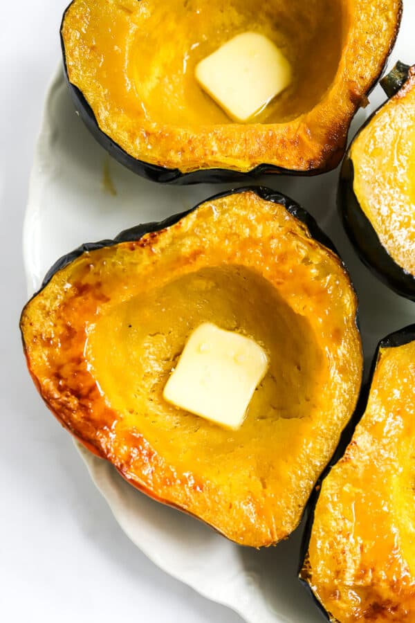 3 pieces of cut acorn squash on a white platter with square pieces of butter on them.