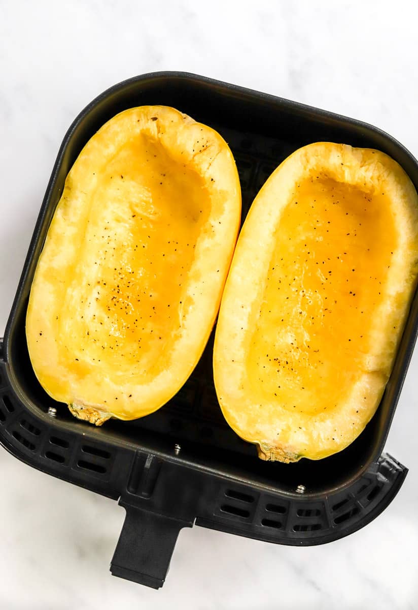 Uncooked squash halves in an air fryer basket. 