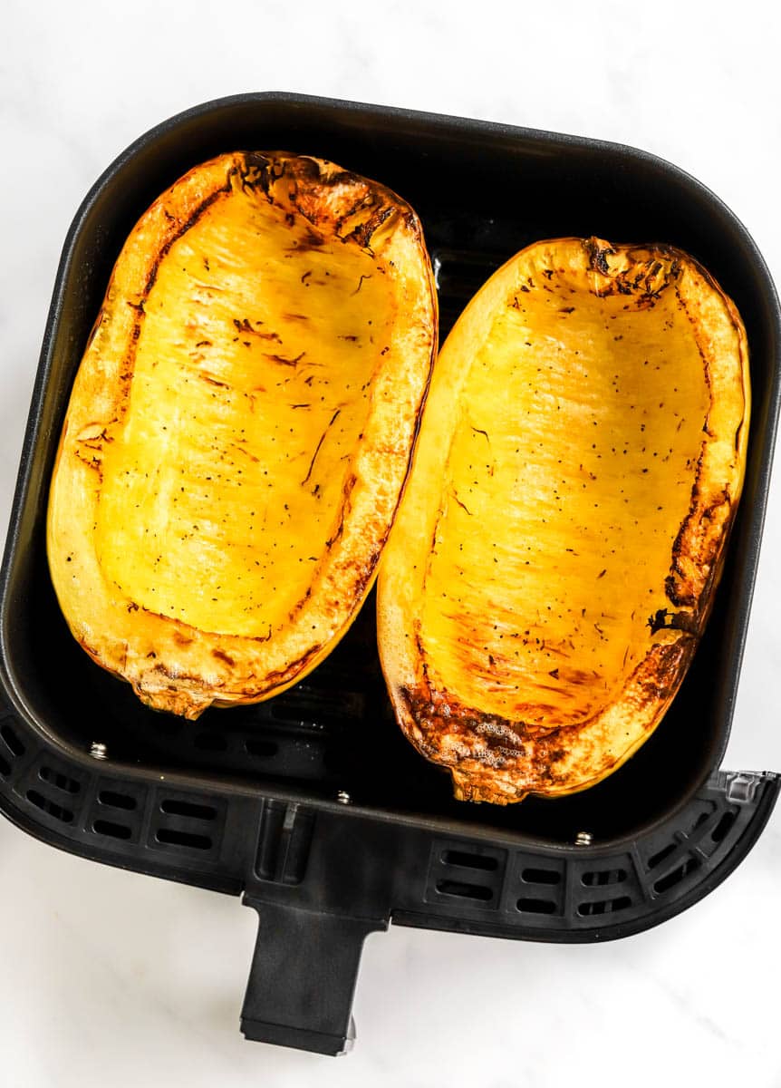 Two halves of roasted spaghetti squash in a black air fryer basket. 