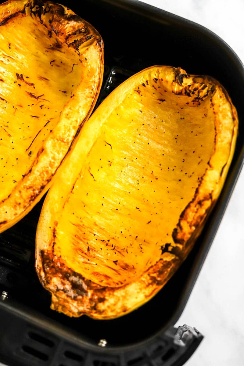 Two halves of spaghetti squash golden and cooked in an air fryer basket. 