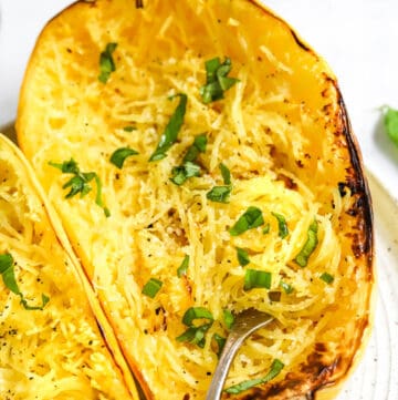 Cur, roasted air fryer spaghetti squash with a fork in it with green herbs on it with another half of squash next to it.