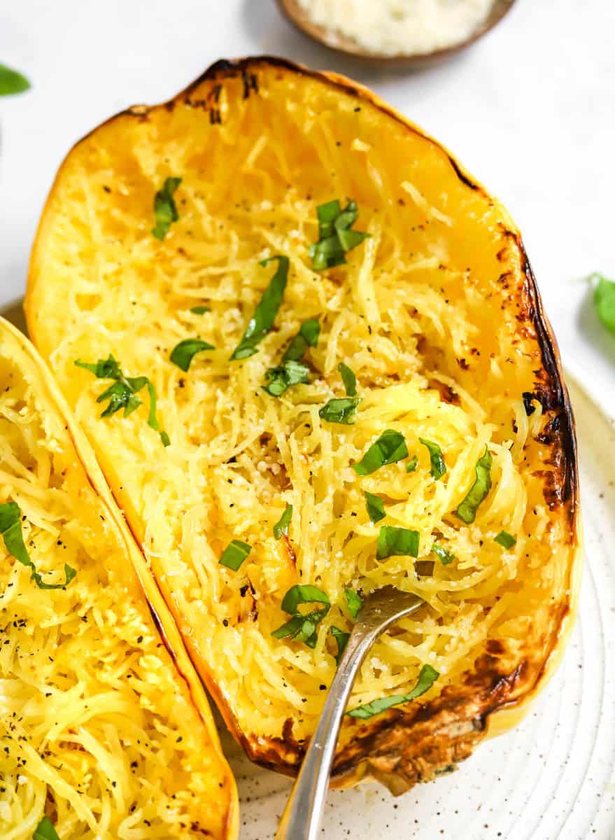 Cut, roasted air fryer spaghetti squash with a fork in it with green herbs on it with another half of squash next to it. 