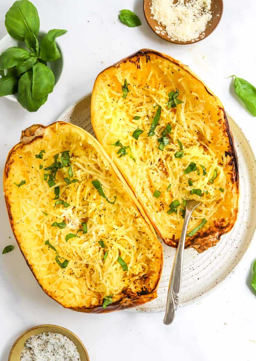 Roasted, halved squash on a plate topped with herbs with a fork inside one of the halves of squash. 