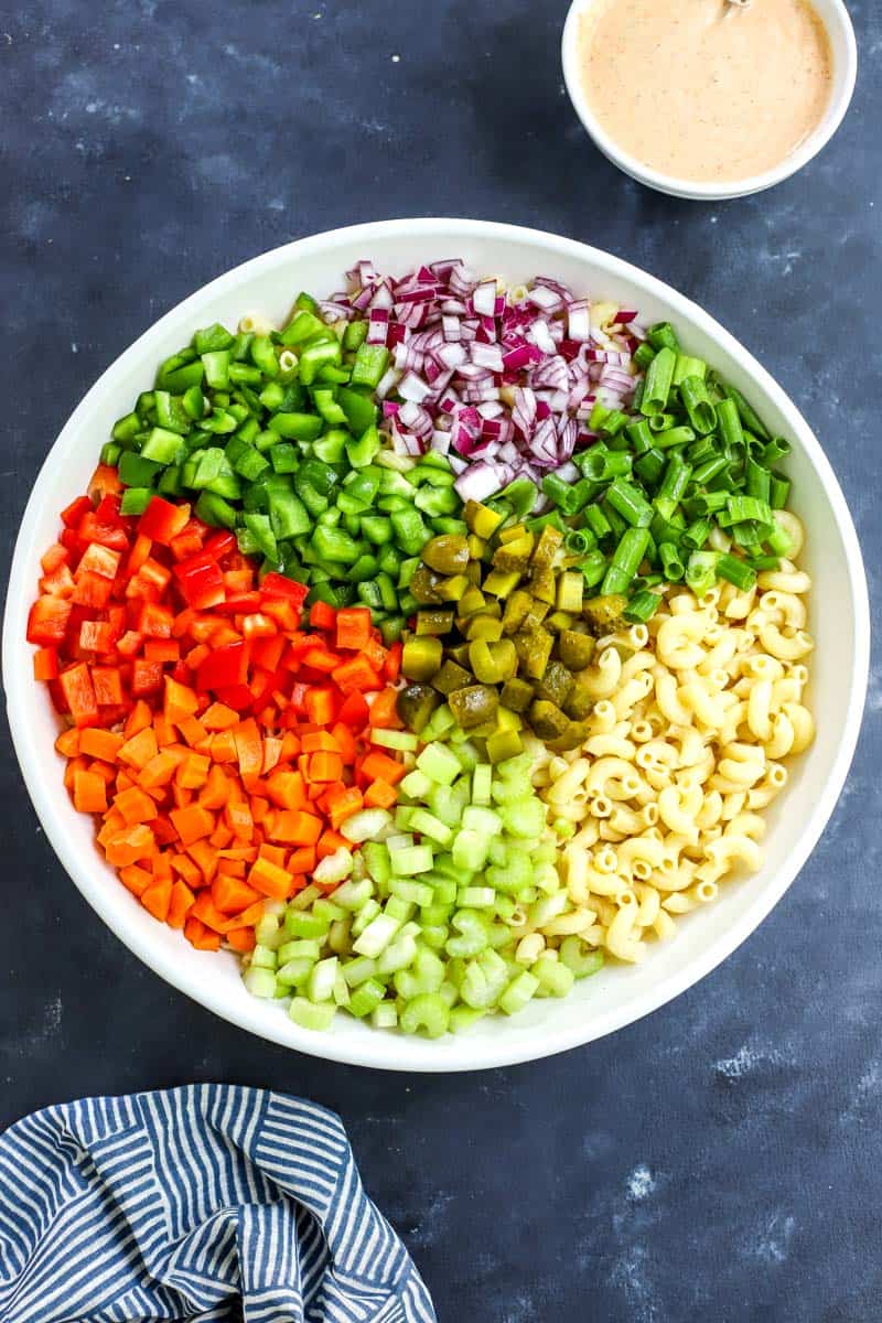 Chopped veggies on a large white bowl with organ dressing in a bowl behind it and a blue and white stripped towel in front of it.