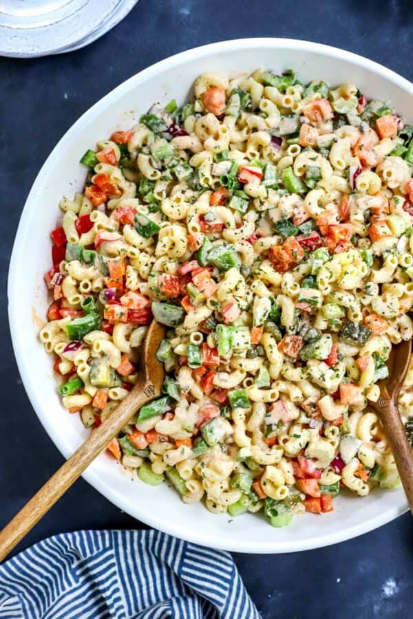 Close up of creamy pasta salad with chopped veggies in it with wooden serving spoons in the bowl.