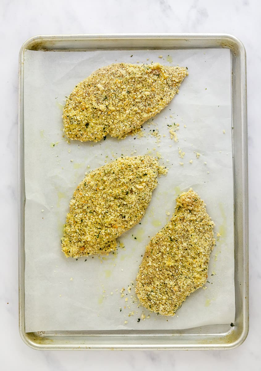 Uncooked breaded chicken cutlets on a lined baking sheet.