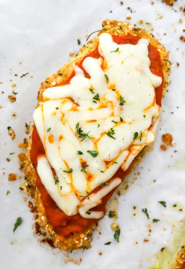 Close up of a piece of chicken Parmesan with gluten free crust on white paper.