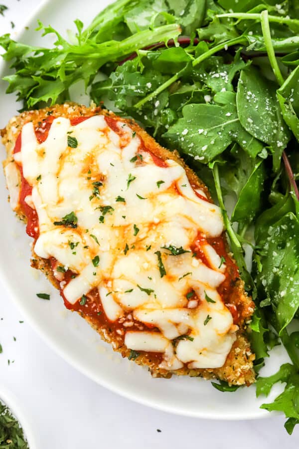 Plate filled with gluten free crusted chicken Parm with mixed greens next to it.