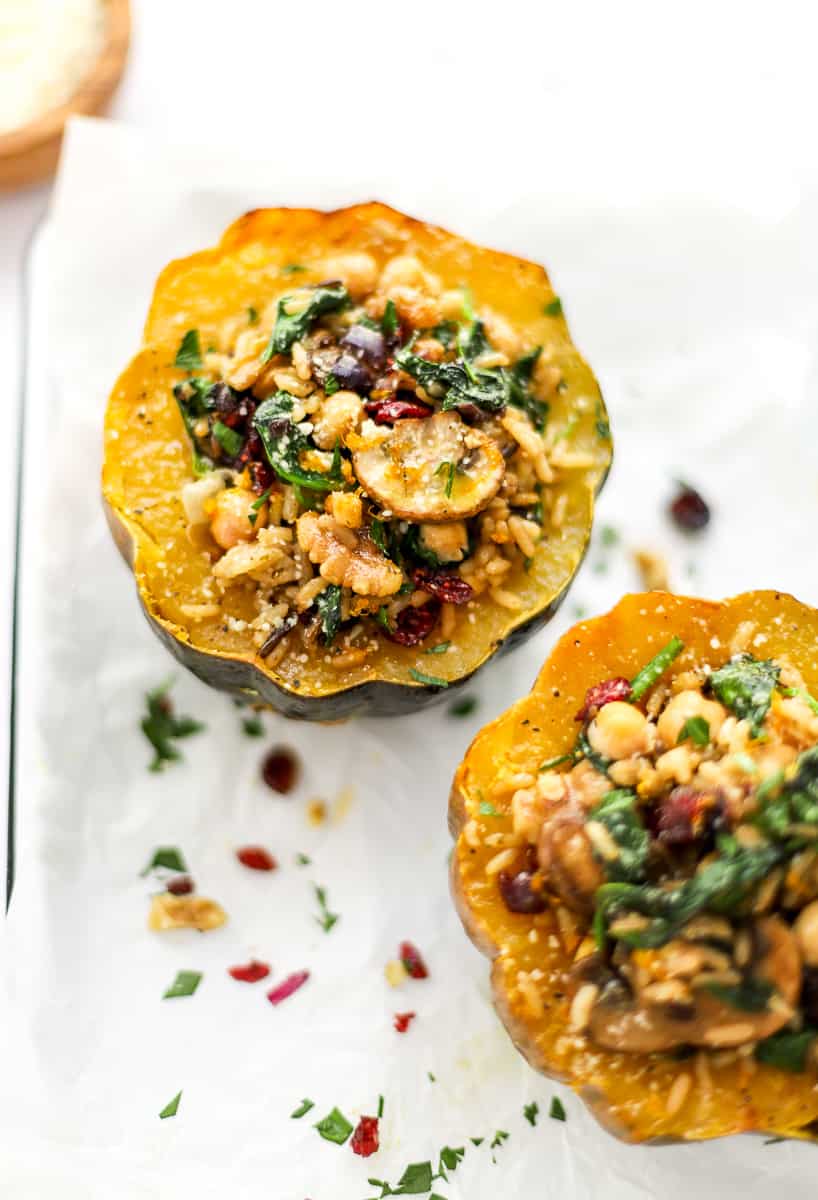 Two acorn squash filled with grains and veggies on a white dish