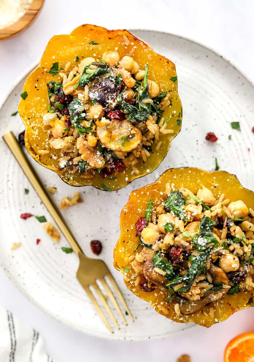 Two stuffed acorn squash on a round plate with a fork on the plate. 