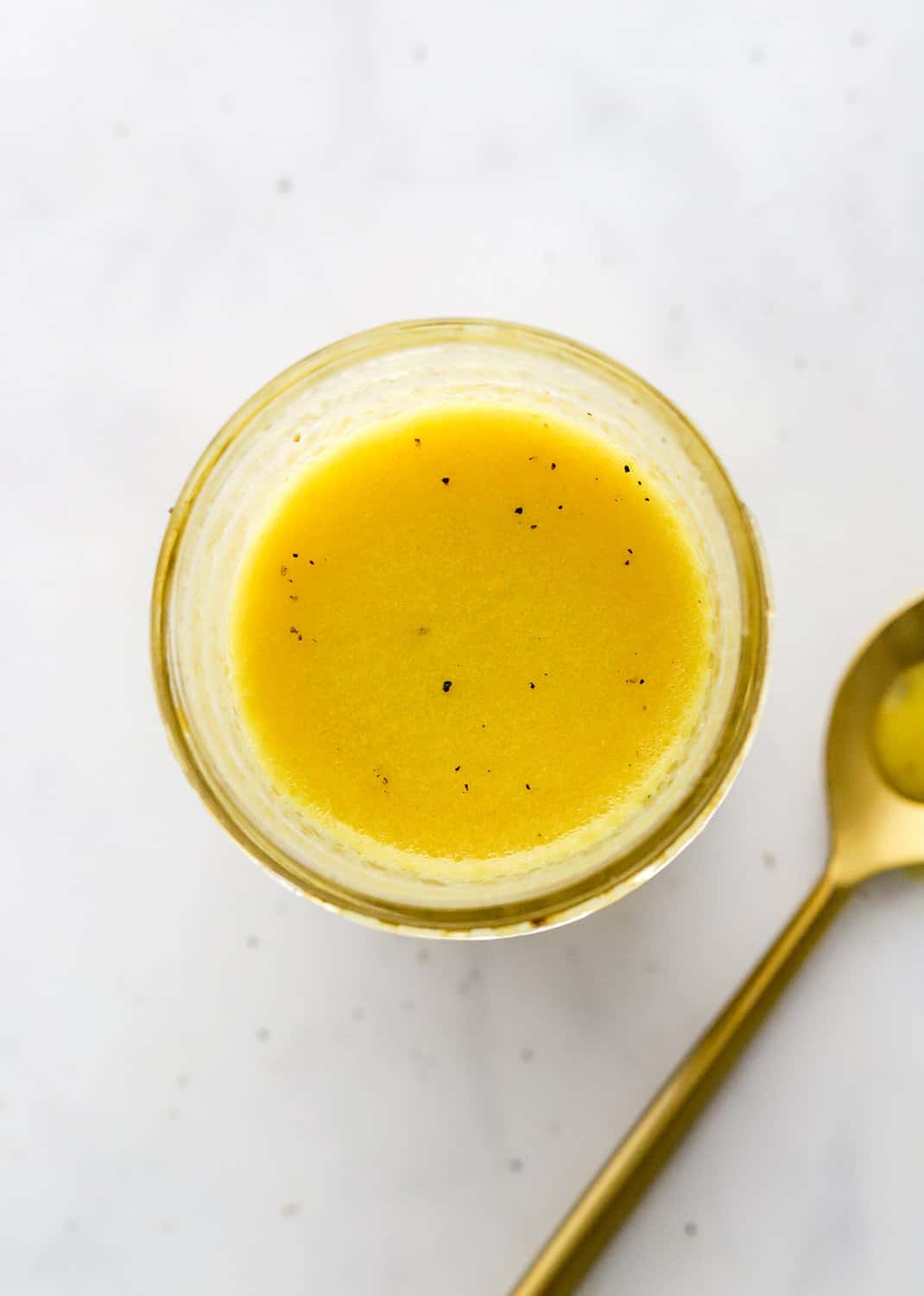 Yellow salad dressing in a mason jar with a gold spoon next to it.