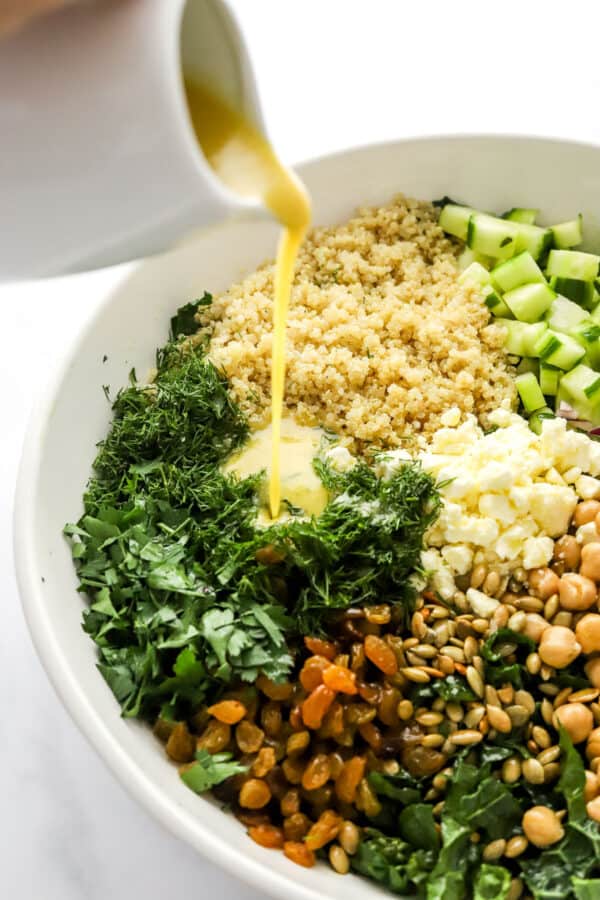 Pouring lemon dressing over a salad with kale and quinoa in it in a white bowl.