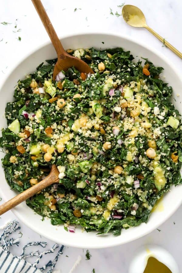 Large white bowl filled with kale and quinoa salad with wooden spoons in it.