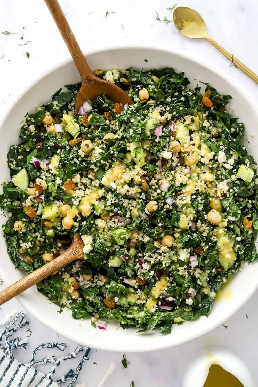 Large white bowl filled dark leafy greens, fresh veggies and grains with wooden spoons in the bowl. 