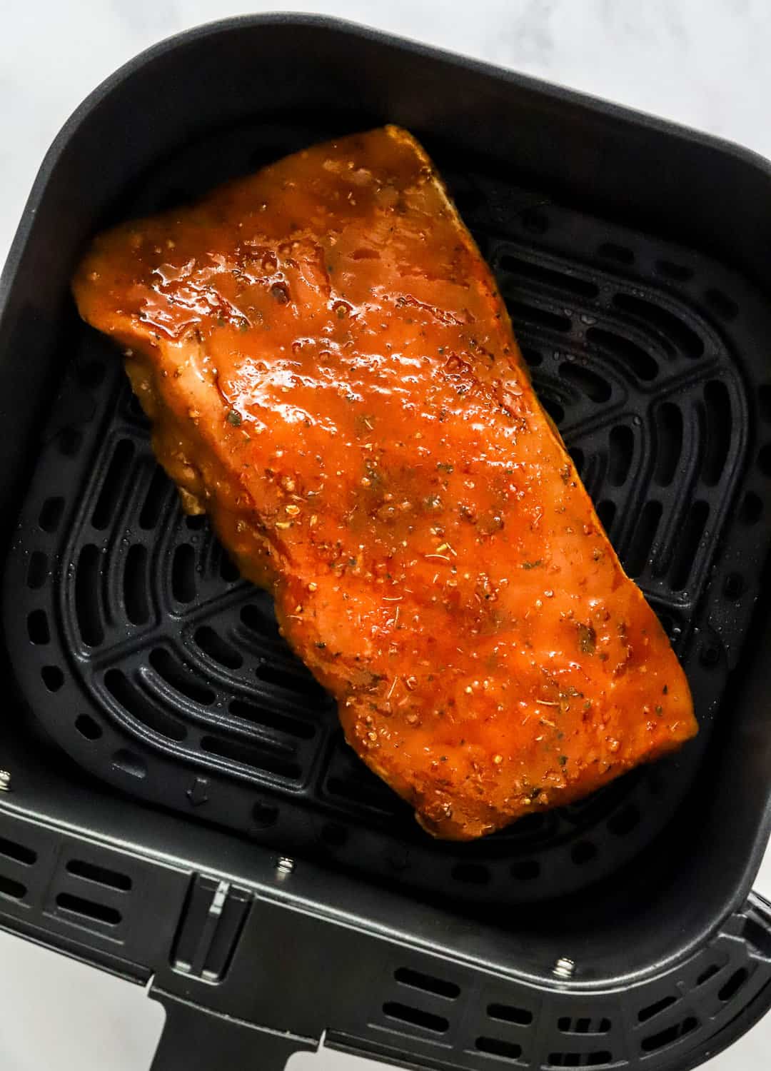Uncooked glazed pork loin in a square air fryer basket