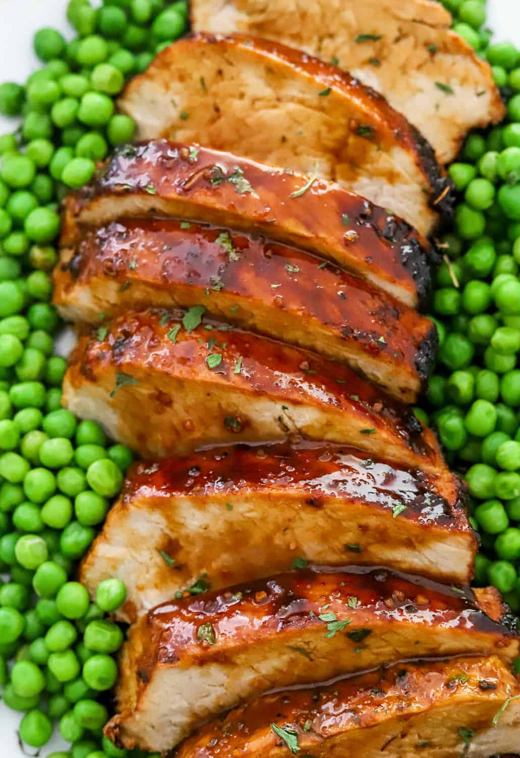 Close up of glazed brown sliced pork with green peas around it.