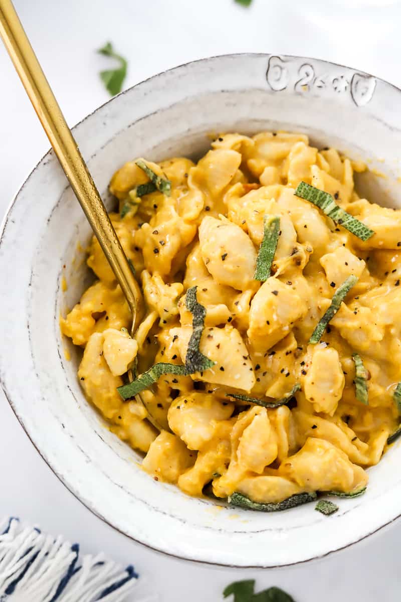 Bowl of cheese shell pasta topped with pepper and herbs with a gold spoon in the bowl.