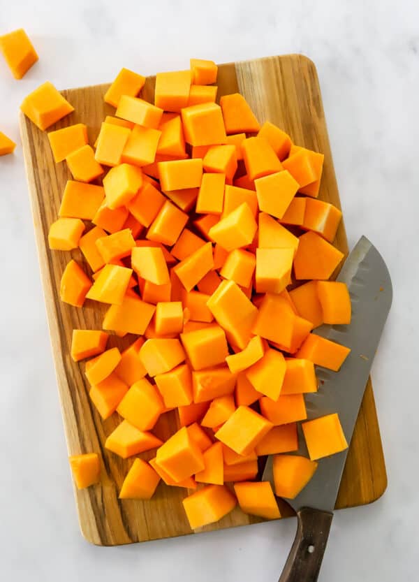 Cubes of cut squash on a wooden cutting board with a knife on the cutting board.