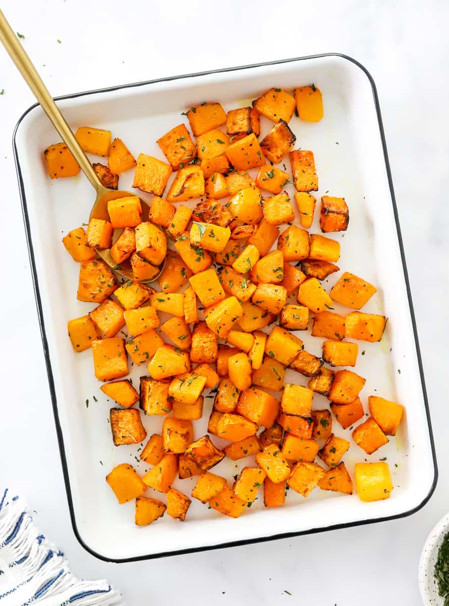 White rectangle tray with roasted squash on it with a gold serving spoon in the tray.  