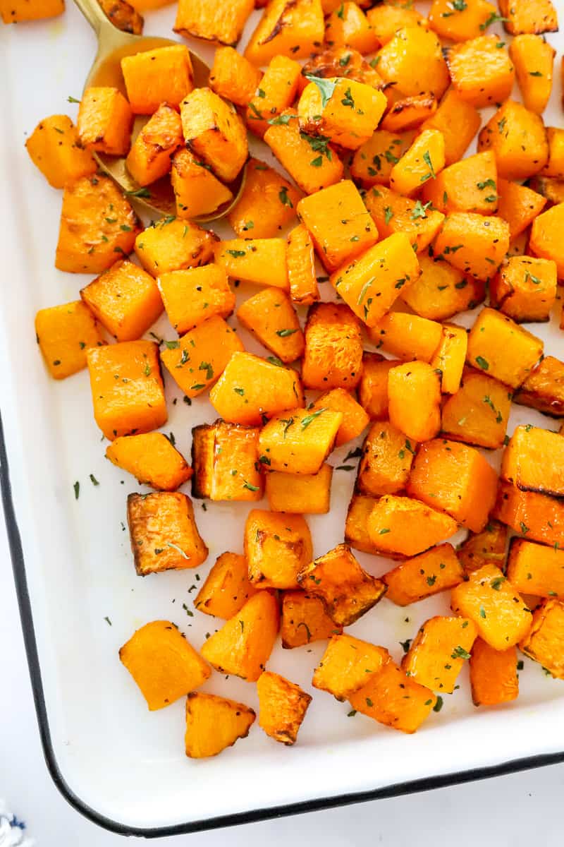 Cubbed air fryer butternut squash on a white platter with a gold spoon in it. 