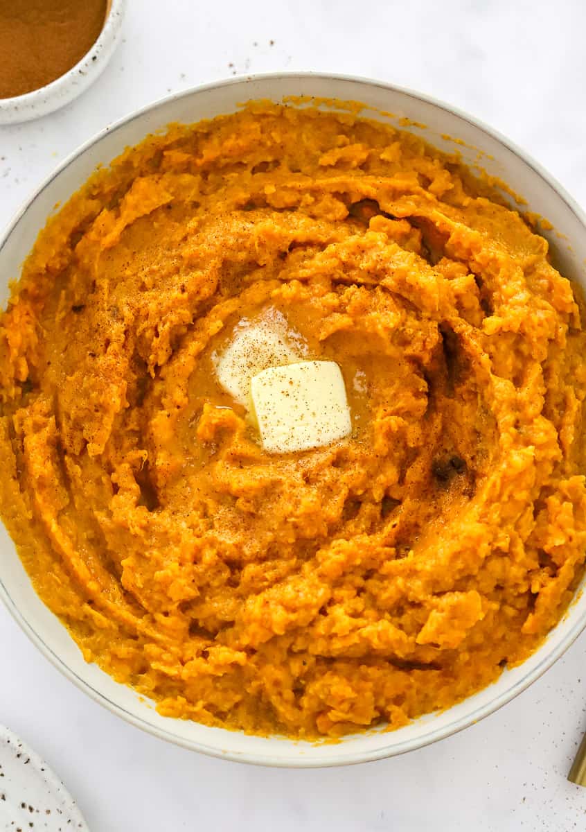 Bowl filled with mashed sweet potatoes with a couple slabs of butter in the middle of it.