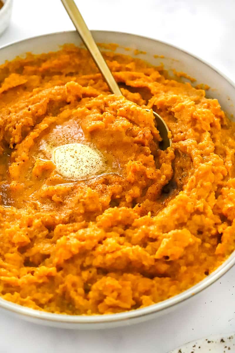 Fluffy mashed sweet potatoes in a serving bowl mixed with butter and cinnamon with a spoon in the bowl. 