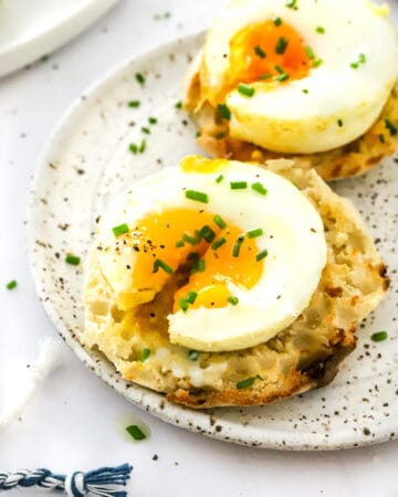Two coated English muffins on a plate with a baked egg on each one with the once in the front cut open.