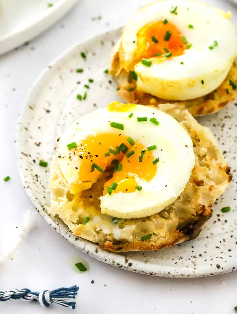 Two coated English muffins on a plate with a baked egg on each one with the once in the front cut open.