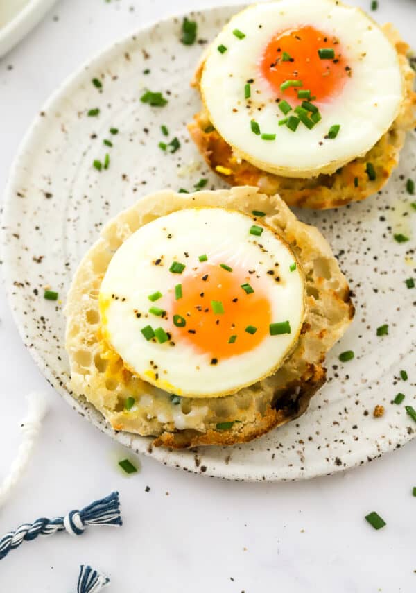 Baked whole eggs on toasted muffin topped with chives on a plate.