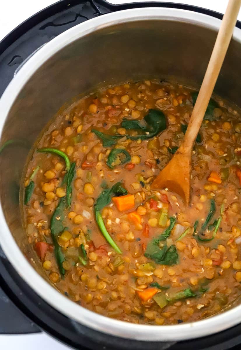 Cooked lentil soup in an instant pot with a wooden spoon in the pot.