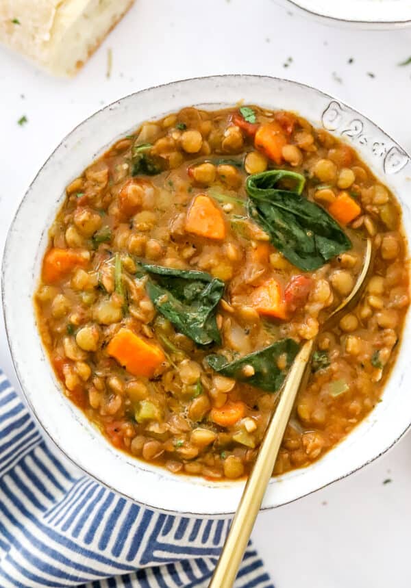 Large bowl of instant pot lentil soup with a gold spoon in the bowl with a white and blue stripped towel in front of it.